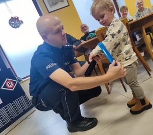 policjant zakładający chłopcu na rękę opaskę odblaskową